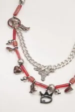Collana decorativa con elementi in metallo e perline rosse, caratterizzata da charms a forma di stivali, cuore e teschio, con una catena argentata e un ciondolo a forma di testa di toro.
