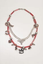 Collana artistica con perline rosse e pendenti metallici, tra cui stivali, cuori e un simbolo di toro, perfetta per un look originale e creativo.