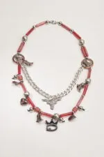 Collana artistica con perline rosse e pendenti metallici, tra cui stivali, cuori e un simbolo di toro, perfetta per un look originale e creativo.
