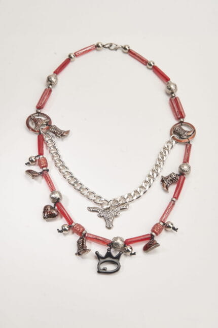 Collana artistica con perline rosse e pendenti metallici, tra cui stivali, cuori e un simbolo di toro, perfetta per un look originale e creativo.