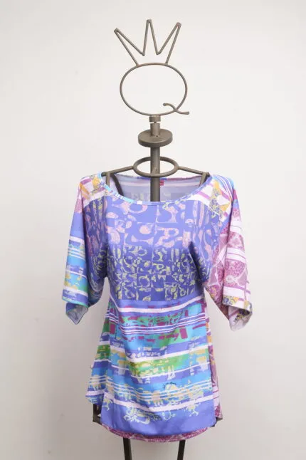 Maglietta colorata con maniche a 3/4 esposta su un manichino, caratterizzata da un design vivace e grafico, ideale per la moda estiva e casual.