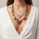 Collana di design unico indossata da una donna, composta da elementi metallici e perline rosse, con charm a forma di cuore, stivale e simboli vari, su sfondo neutro.