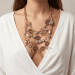 Collana elegante e multi-strato indossata da una donna con maglietta bianca, caratterizzata da perline e dettagli in tonalità neutre. L'accessorio aggiunge un tocco di stile e raffinatezza al look.