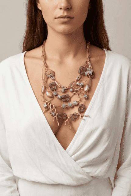Collana elegante e multi-strato indossata da una donna con maglietta bianca, caratterizzata da perline e dettagli in tonalità neutre. L'accessorio aggiunge un tocco di stile e raffinatezza al look.