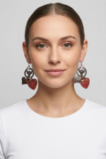 Orecchini a forma di cuore rossi e argento indossati da una donna, con un top bianco, su sfondo grigio chiaro. Accessorio di moda che aggiunge un tocco elegante e moderno al look.