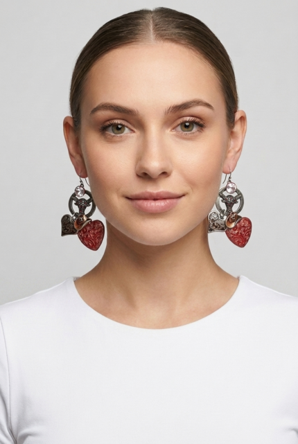 Orecchini a forma di cuore rossi e argento indossati da una donna, con un top bianco, su sfondo grigio chiaro. Accessorio di moda che aggiunge un tocco elegante e moderno al look.