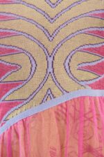 Dettaglio del vestito in maglia jacquard e tulle, caratterizzato da una stampa a fiori vivace e un design elegante. La parte superiore presenta un motivo geometrico in tonalità gialle e rosa, mentre la parte inferiore è realizzata in tulle leggero.
