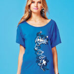 Modella che indossa un abito corto bluette con ricami e applicazioni artistiche, su sfondo azzurro. Abbigliamento elegante e alla moda, perfetto per occasioni estive. 