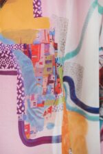 Dettaglio di un kaftano in tulle elasticizzato con una stampa colorata e vivace, caratterizzato da motivi geometrici e astratti che richiamano tonalità di blu, arancione, giallo e rosa. Ideale per un look estivo e alla moda.