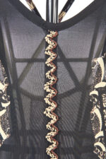 Dettaglio del retro di un abito lungo nei toni beige, marrone e nero, con ricamo decorativo e stampa elegante. Il colletto presenta un design particolare con una cucitura a zigzag in tonalità contrastanti.