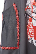 Dettaglio di una tunica con stampa floreale, evidenziando una tasca con bordatura rossa e nera su fondo grigio. Perfetta per uno stile elegante e alla moda.
