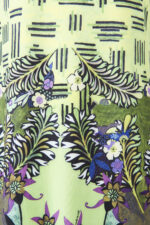 Dettaglio di un vestito a fantasia con motivo floreale e foglie su sfondo verde chiaro, ideale per l'estate e per occasioni casual.