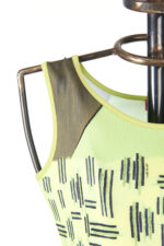 Dettaglio di un vestito a fantasia verde con motivi geometrici, esposto su un manichino. Il design presenta spalline larghe e un mix di colori vivaci, ideale per la moda estiva.
