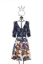 Abito a fantasia con top blu scuro a maniche corte e gonna stampata in tonalità di blu e arancione, esposto su un manichino. Perfetto per occasioni estive e look casual.