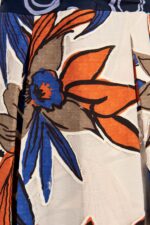 Dettaglio di un vestito con tessuti devorè, caratterizzato da un motivo floreale in tonalità arancione, blu e grigio su sfondo chiaro, evidenziando la texture unica del tessuto.