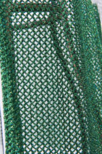 Dettaglio di un tessuto a rete verde brillante utilizzato per un cardigan, evidenziando la trama e la lucentezza del materiale.