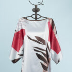 Blusa stampata con maniche ampie e design floreale, caratterizzata da tonalità di rosso, marrone e bianco, esposta su un manichino su sfondo azzurro.