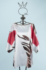 Blusa stampata con maniche ampie e design floreale, caratterizzata da tonalità di rosso, marrone e bianco, esposta su un manichino su sfondo azzurro.