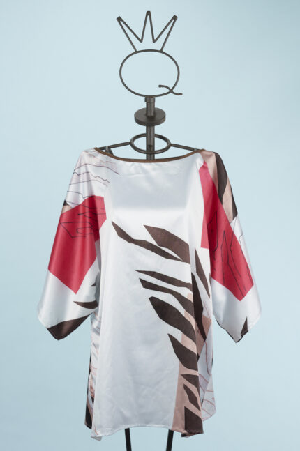 Blusa stampata con maniche ampie e design floreale, caratterizzata da tonalità di rosso, marrone e bianco, esposta su un manichino su sfondo azzurro.