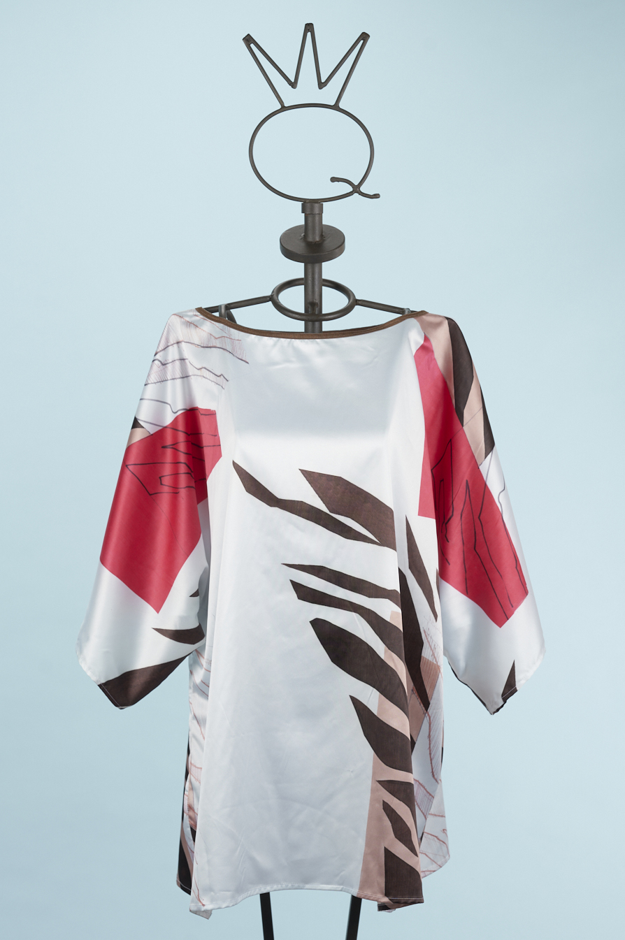 24SSQ1422_A Blusa stampata con maniche ampie e design floreale, caratterizzata da tonalità di rosso, marrone e bianco, esposta su un manichino su sfondo azzurro.