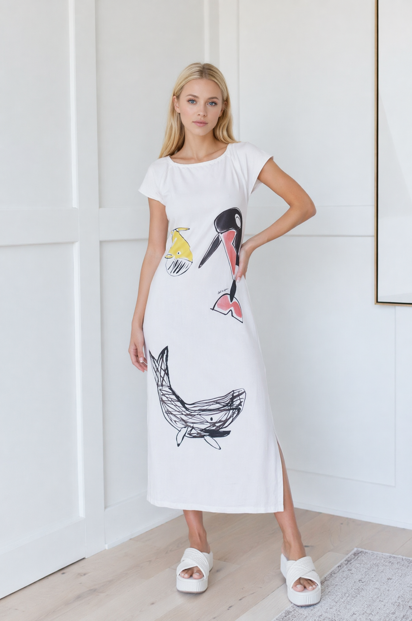 18SSNB46001 Modella che indossa un vestito lungo bianco con stampe artistiche di pesci e uccelli, abbinato a sandali bianchi, in un ambiente moderno e luminoso.